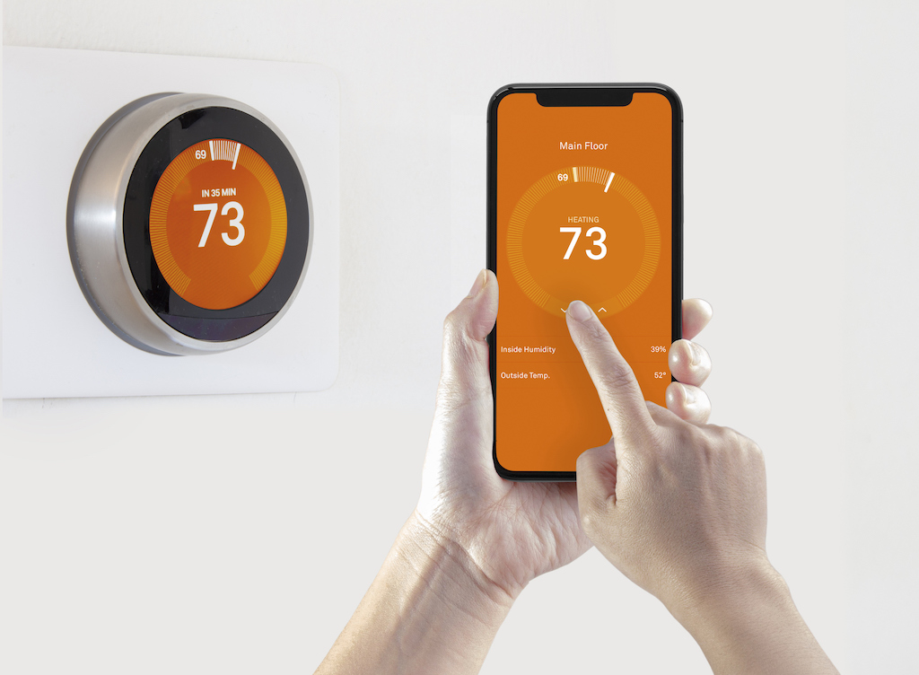 A person using a smart phone application warming up the room temperature with a wireless smart thermostat on a white background. Air conditioning service