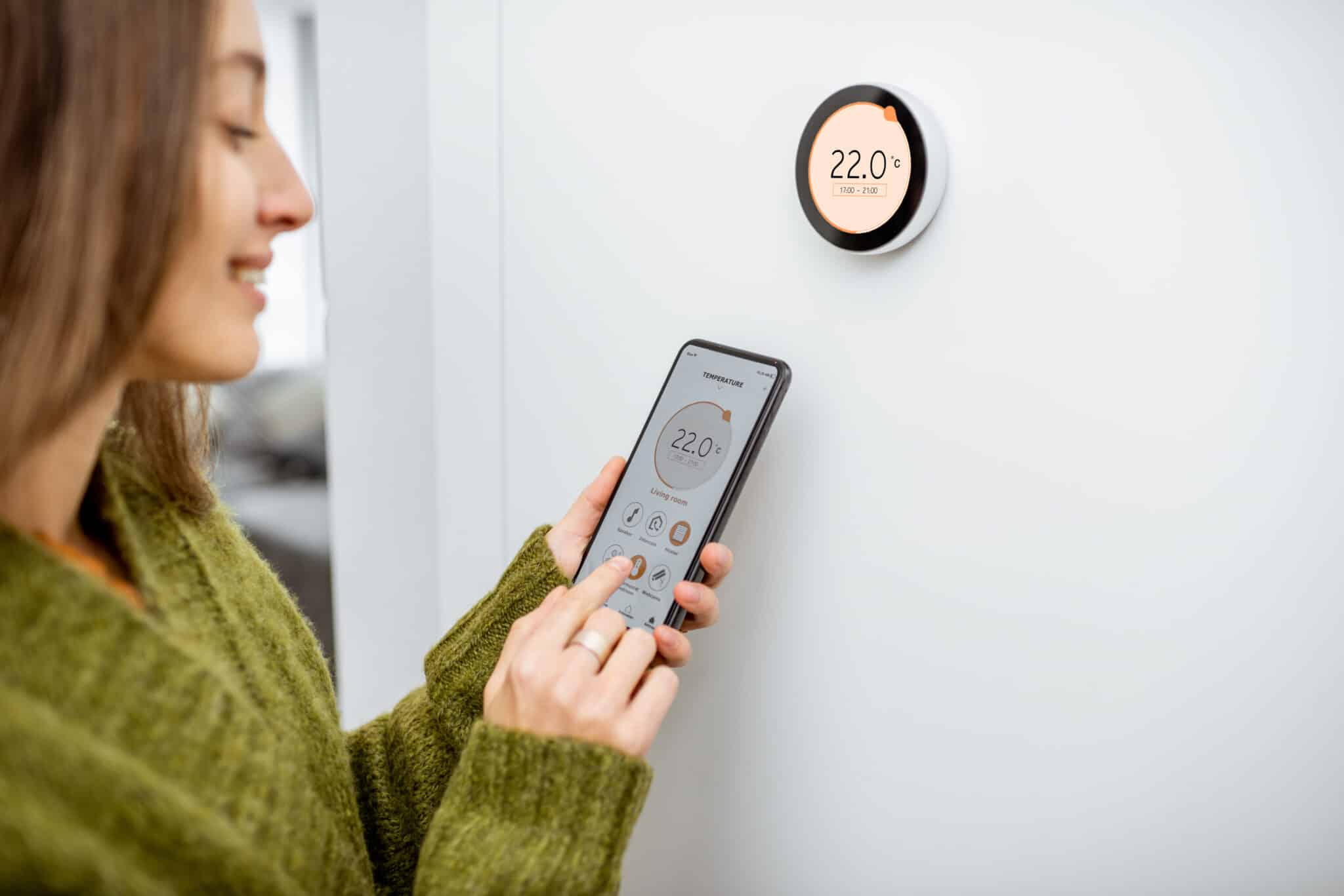 A woman adjusting Smart Thermostat Settings to regulate the heating temperature using her phone.