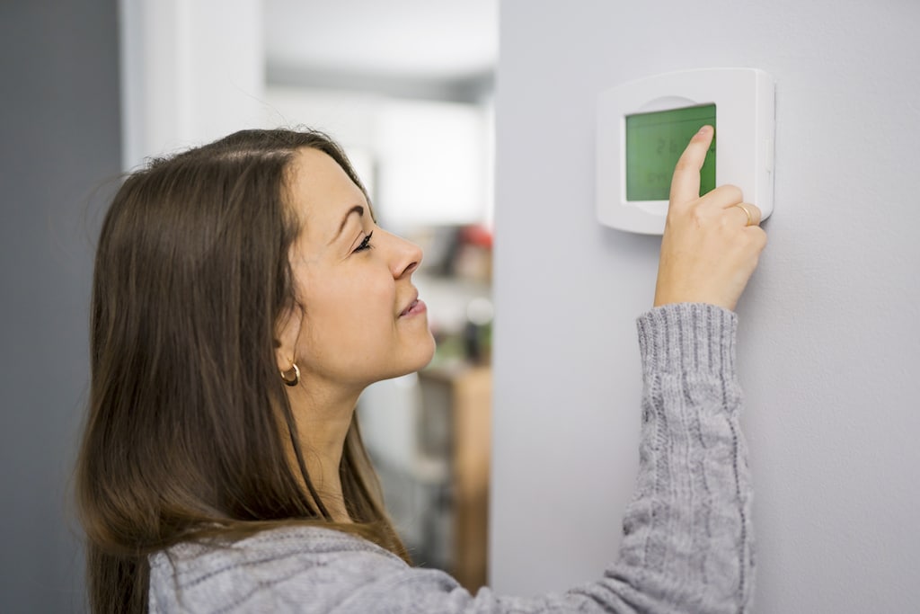 A woman set the thermostat at house. | Emergency Heating and AC Repair Service