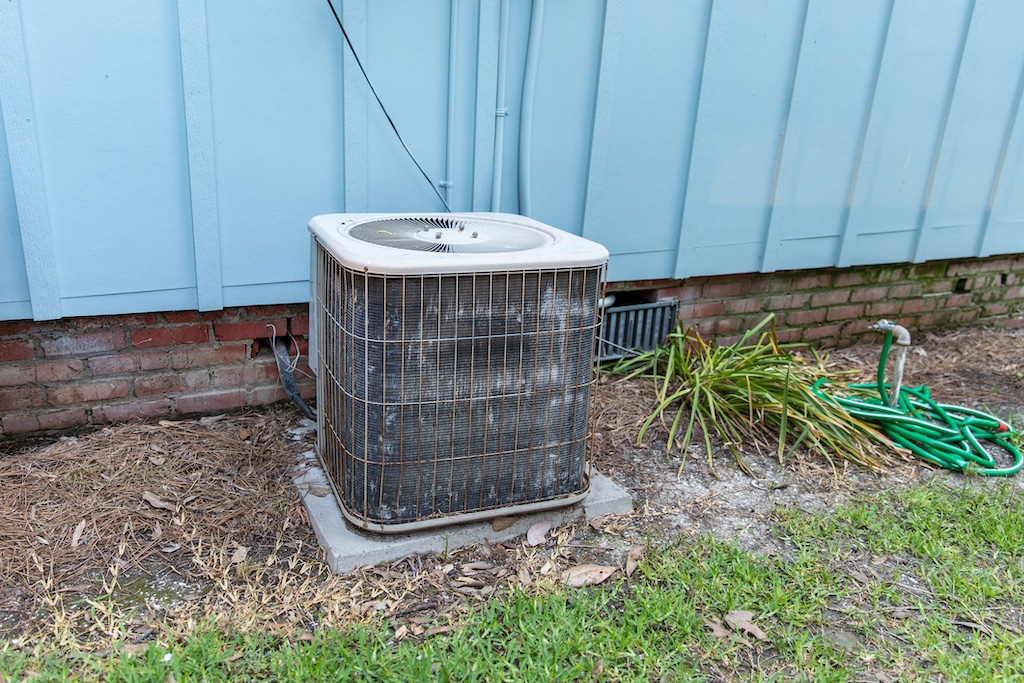 Old air conditioner system compressor next to home, needing maintenance.| Emergency Heating and AC Repair Service