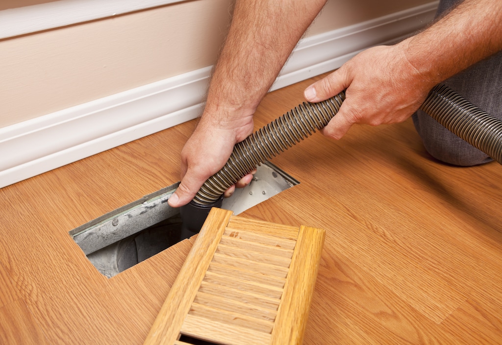 Person cleaning floor duct, in need of Duct Cleaning Service