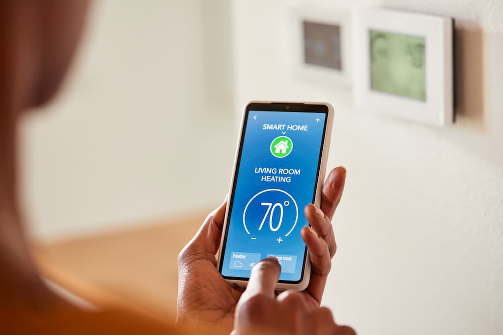 Woman holding phone controlling the ac through a smart home device. Air Conditioning for Homes with Boilers.