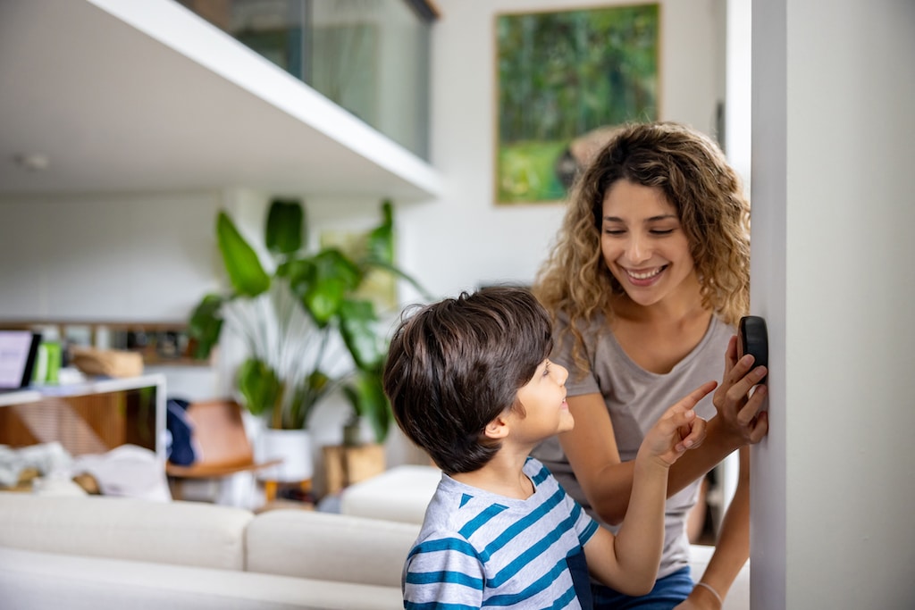 Mother and son adjusting thermostat with natural background. Natural Gas Heating and Cooling Systems.