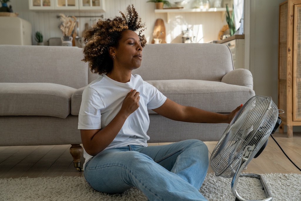 Woman using fan during AC outage during hot Texas summer, in need of AC repair.