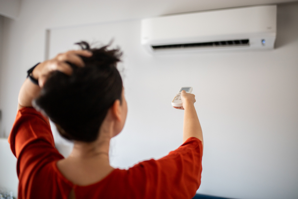 Woman adjusting ac unit with remote | Air Conditioning Service