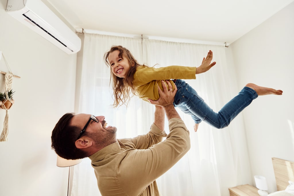 Father and daughter playing in living room with ac unit on wall. | Residential HVAC Code Requirements