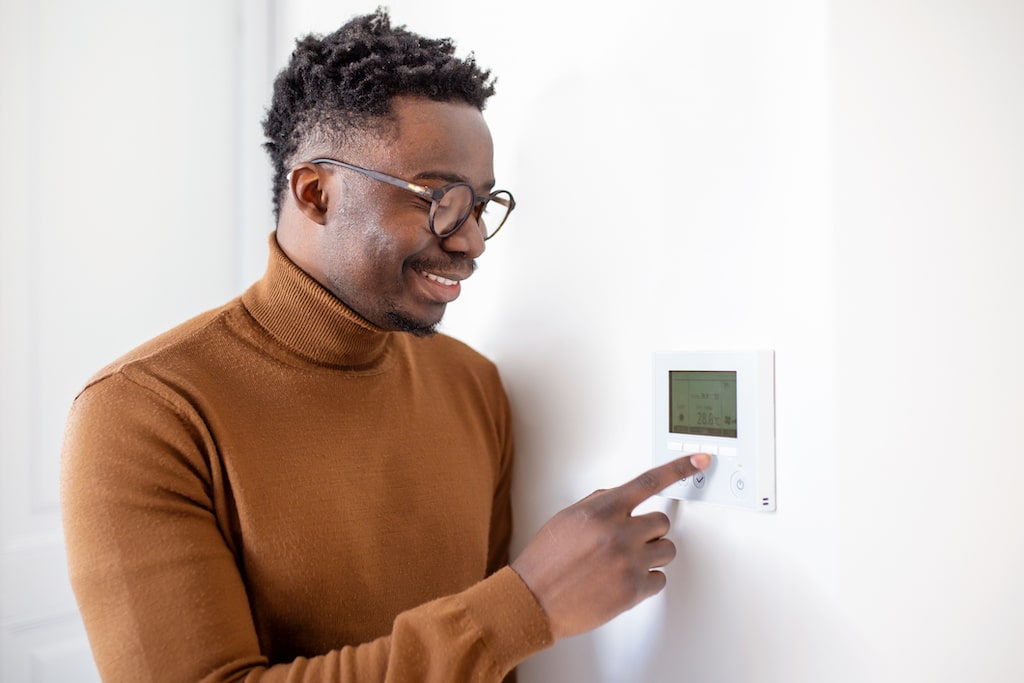 Man in sweater adjusting temperature on thermostat. | Heating Strips for HVAC