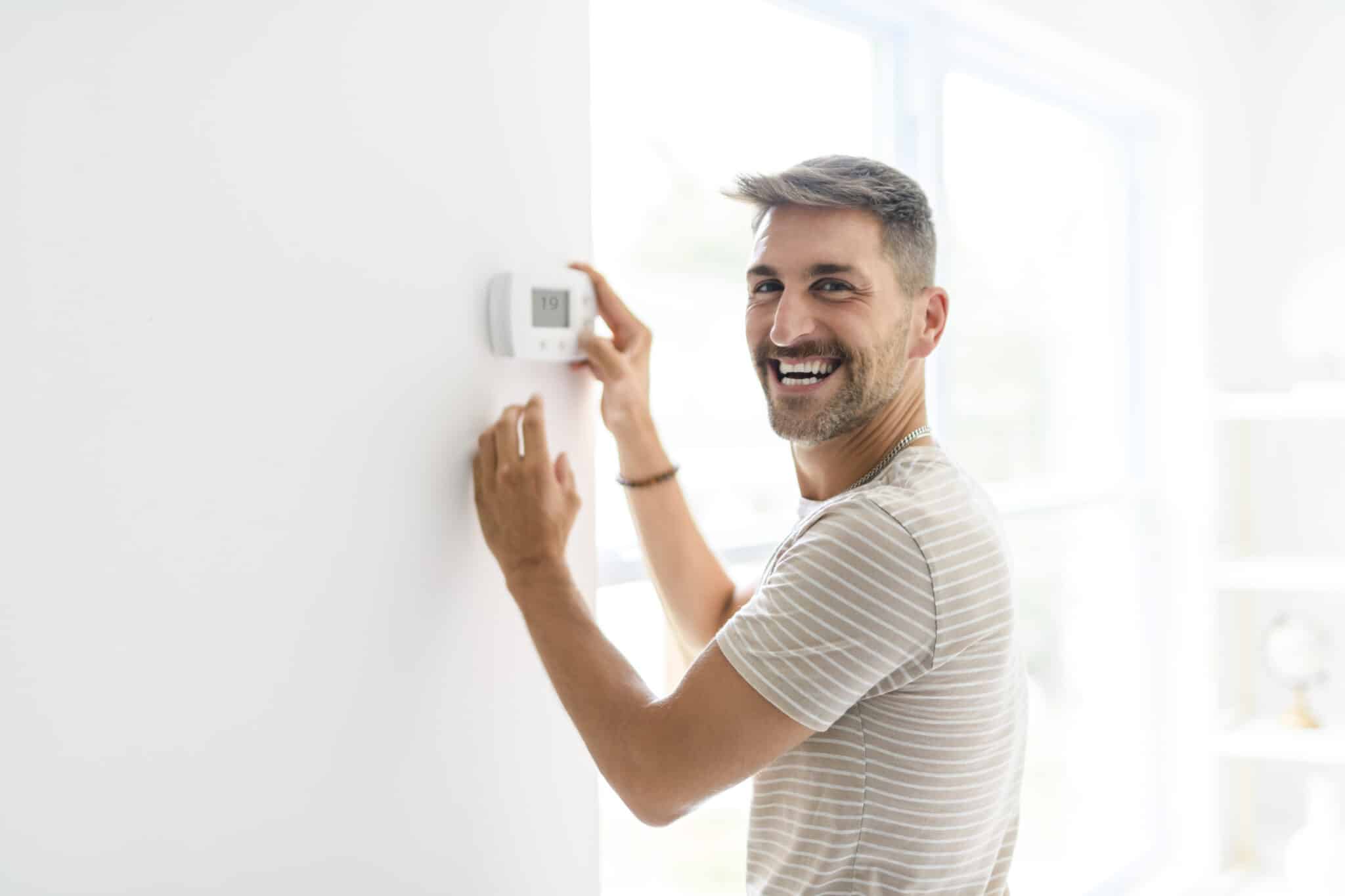 Smiling man adjusting thermostat, HVAC.