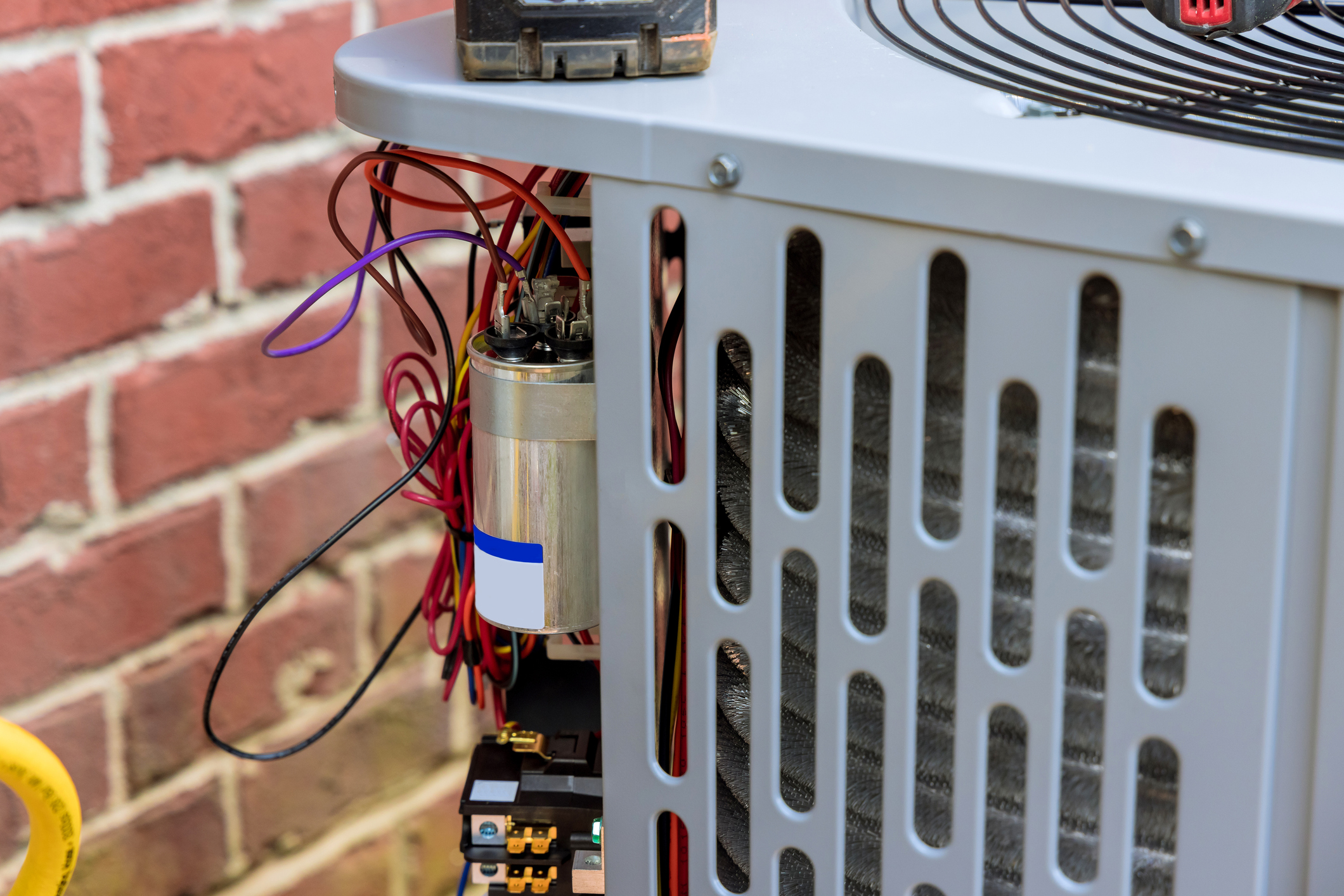 HVAC technician performing a start capacitor test and repair on an outdoor AC unit.