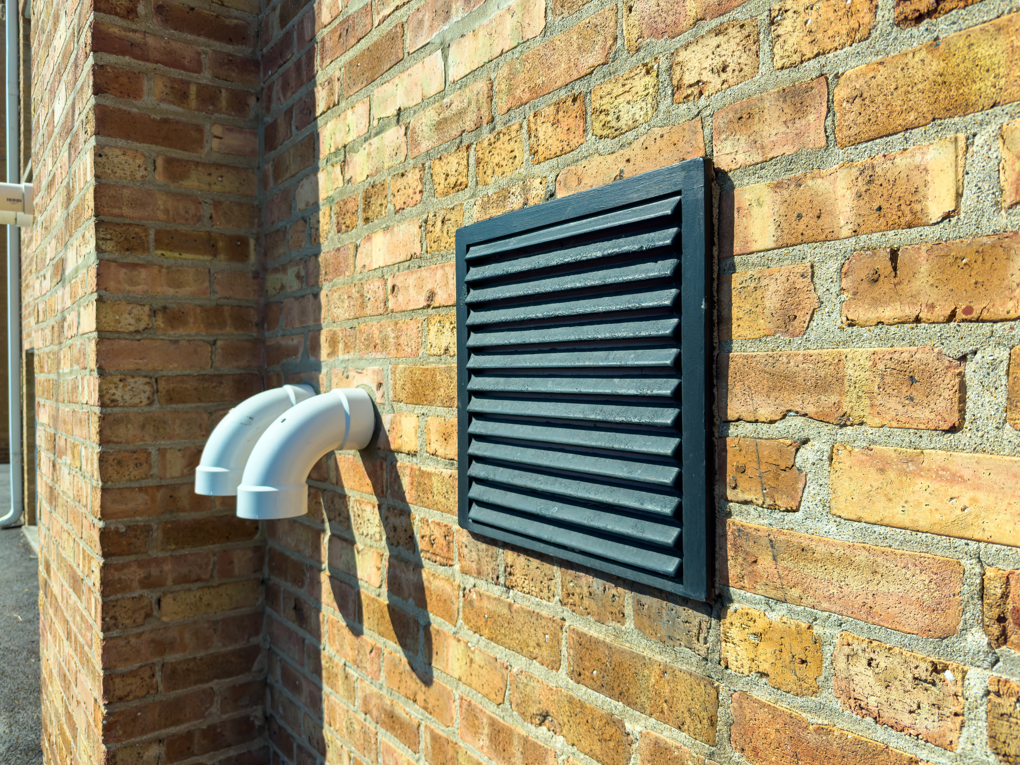 Outside air intake ventilation system installed on a brick exterior wall in an urban setting, with pipes connected to the building.