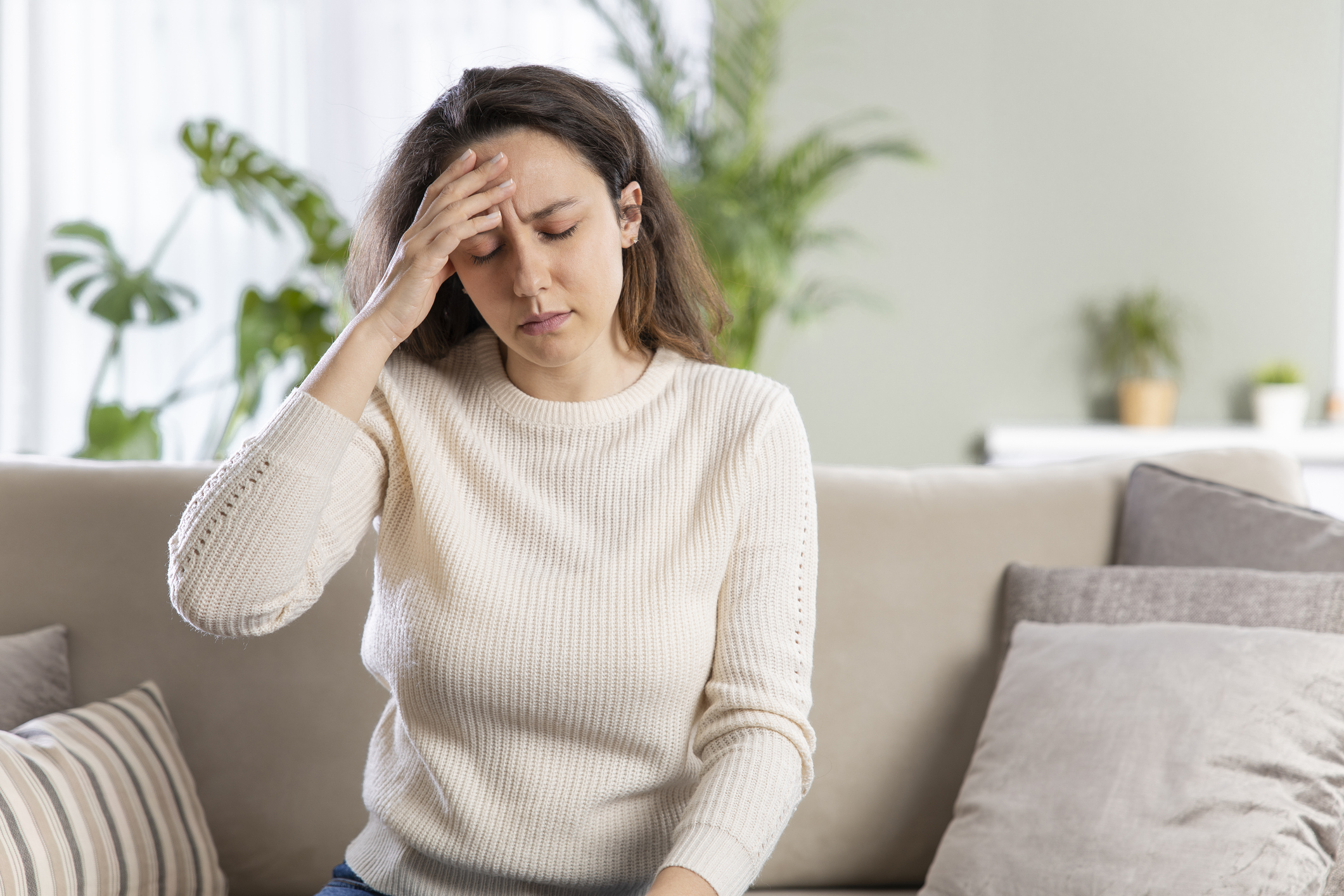 Combustion air problems at home, Young woman with headache sitting on sofa, Combustion air sizing.