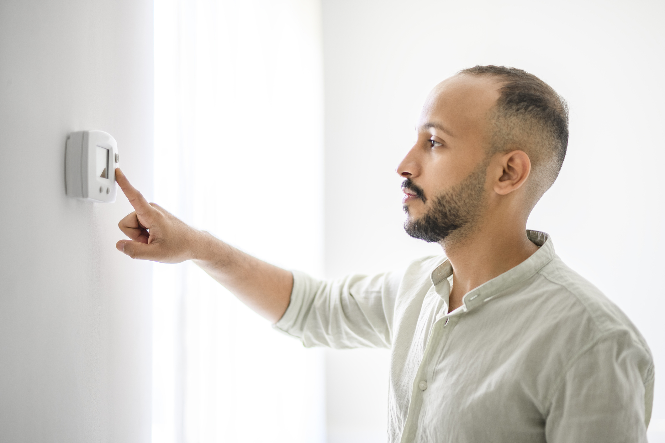 Man adjusting room temperature with electronic thermostat at home, Thermostat schedule programming.