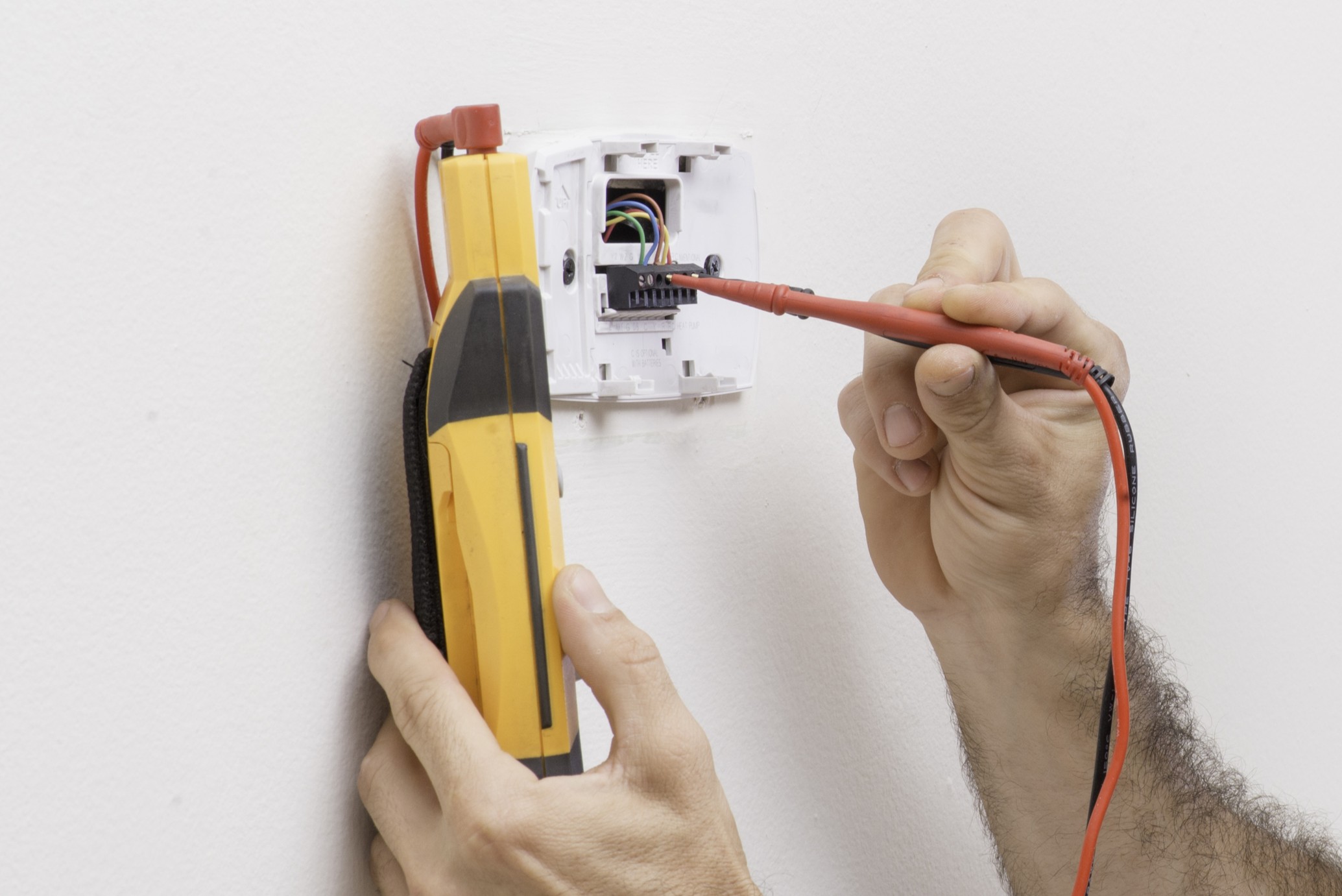 HVAC tech checking low voltage on a thermostat, HVAC equipment problems.